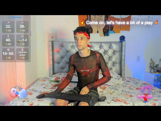 Franchessco69, een slanke jonge man met kort donker haar, die een rode hoofdband draagt en een doorschijnend zwart shirt, zit op een bed en houdt een toetsenbord vast. Zijn achterkant is zichtbaar..