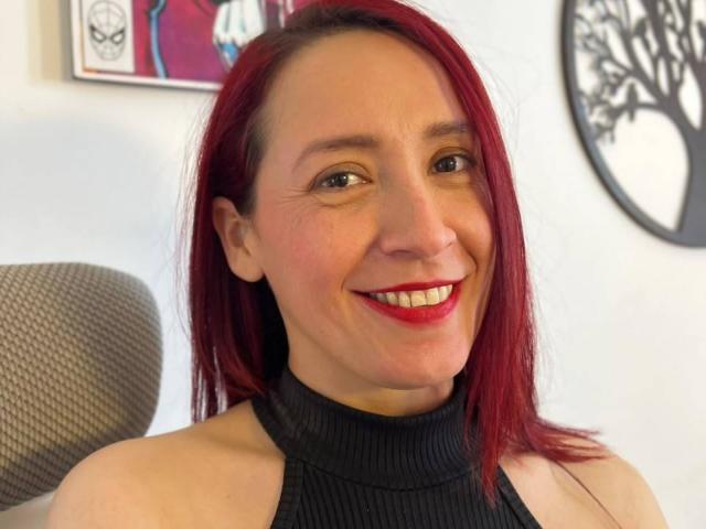 SweettEve with red hair, smiling, wearing a black ribbed turtleneck, showing her ass-free upper body and red lipstick. She's got a cute, happy face.