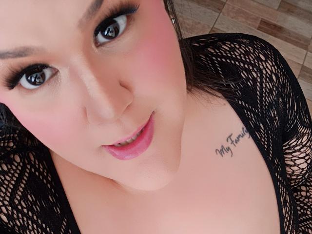 GiiannaMorrys has pink blush on her cheeks, black eyeliner, and pink lipstick. She's wearing a black netted top, and has a tattoo on her right chest that reads "My Family".