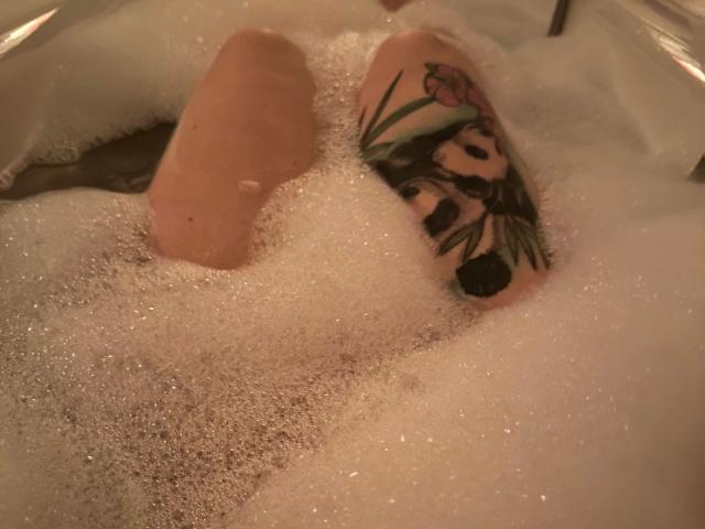 Greekmadame1-hot's leg with a colorful tattoo of a girl and green leaves, submerged in bubbly water. Only the leg and tattoo are visible.