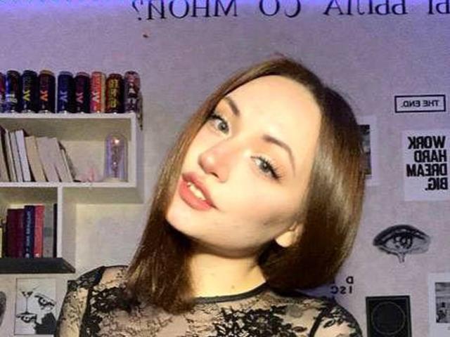 LelaTraverso has light skin, brown hair, and wears a black lace top, looking slightly to the side with a subtle smile and pink lipstick.