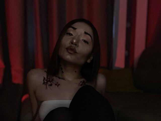 LelaTraverso with bloody star tattoos on her chest, dark brown bob, pouty lips, wearing a strapless white top, black thigh-highs, dim red lighting, looking slightly down.