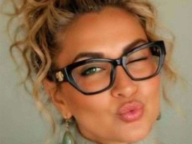 ChaudeEvely has curly blonde hair, big black glasses, and is making a pouty face with her green eyes winking. Her ass is not visible.