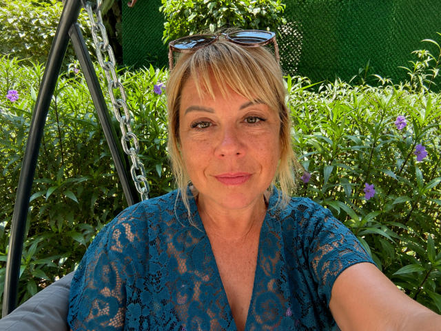 ChristinaDavedes has blonde hair, blue lace shirt, and sunglasses on head, smiling with pink lips, medium-sized tits, and green-eyed, sitting in a swing in a sunny garden.