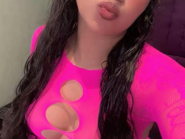 JeimyCampos with dark wavy hair, pouty pink lips, and a hot pink mesh top with large circular cutouts revealing her big tits. She's making a kissing face.