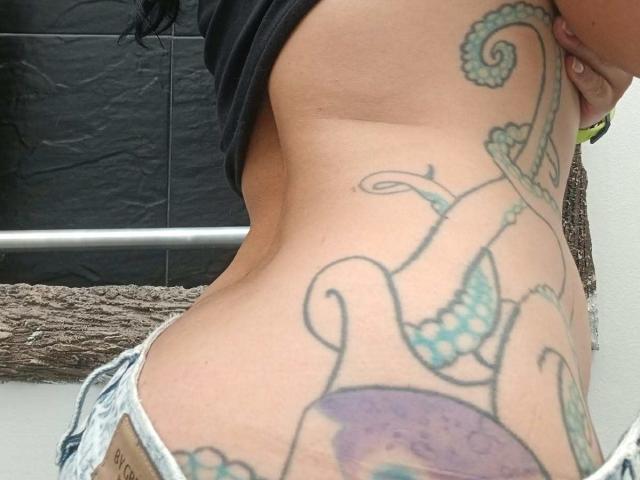 ZarayFeet's side tattoo, showing colorful octopus and swirling lines, with denim shorts and black shirt, exposing a slim, tan waist and visible lower back.