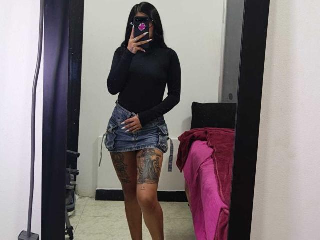 LuciadelaVega has tattoos on her thigh, black long-sleeve top, denim mini-skirt, and is taking a mirror selfie, showing her ass, with a phone covering her face.