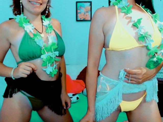 LunaVenus wearing green bikini, black fringed bottom, green-white lei, and LunaVenus in yellow bikini with white fringed bottom, yellow-white lei, holding green can. Both have visible tits.