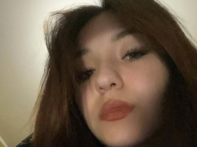 AletaBreslauer has pale skin, dark brown hair, and is pouting with red lipstick. Her eyelashes are long and she's looking slightly to the side. Her nose is small.