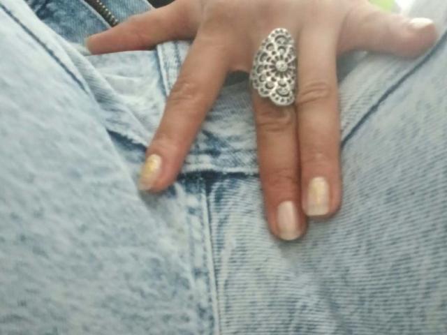 ZarayFeet's hand with a large, ornate silver ring on her pinky, resting on her blue denim jeans, showing her neatly manicured nails.