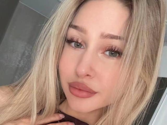 MilagrosEdmisten has blonde hair, green eyes, and full pink lips. She's looking at the camera with a slight smile, showing off her long eyelashes and groomed eyebrows.