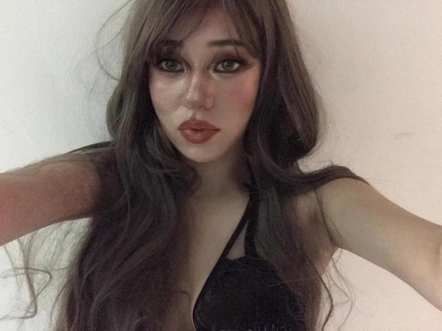 RaniaRem with long brown hair, dark eyeliner, and red lipstick, wearing a black halter top, showing off her tits and a sexy, pouty face in a selfie.