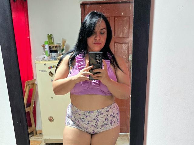 VivianaThompson, with black hair, purple top, and purple butterfly panties, stands in front of a mirror, holding a phone, showing her tits and ass.