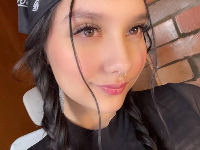 Jade Palacios mit schwarzen Zöpfen, pinkem Lippenstift, Nasenring und einem schwarzen Stirnband, lächelt in die Kamera. Ihr Hintern ist nicht sichtbar, nur ihr Gesicht..