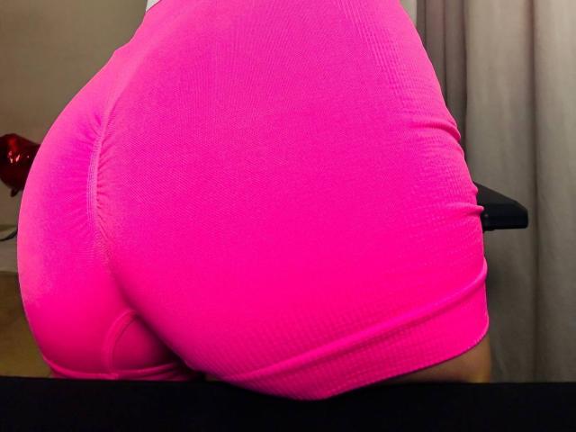 BalletSwan's bright pink ass is prominent in the photo, showing tight, shiny fabric that highlights her round, voluptuous butt. A red object is partially visible on the left.