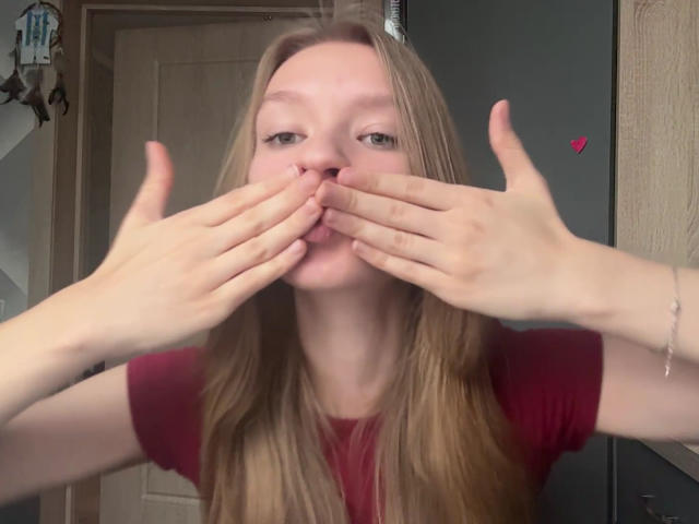 ColeneBeauharnois has long blonde hair, pale skin, and is making a duck face with her hands covering her mouth. She wears a red shirt, and a small pink heart is visible.
