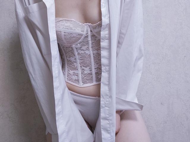 La peau claire de SheritaChieng, ses petites seins, et son corset en dentelle blanche assorti à une chemise et des sous-vêtements blancs, sa chemise ouverte pour révéler sa poitrine et son ventre, debout contre un mur..