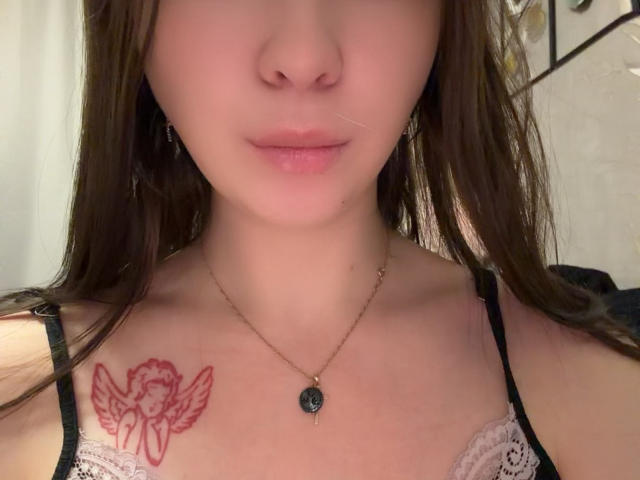 HottiePurdum, avec sa peau claire, ses cheveux bruns et ses lèvres roses, porte un haut en dentelle noire, et a un tatouage d'ange rouge sur sa poitrine droite, ainsi qu'un collier en or..
