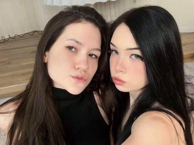 LornaAndGerry, deux jeunes femmes asiatiques mignonnes avec de longs cheveux noirs, portant des hauts noirs, se tenant près l'une de l'autre, les deux regardant l'appareil photo avec les lèvres légèrement entrouvertes, montrant leurs seins..