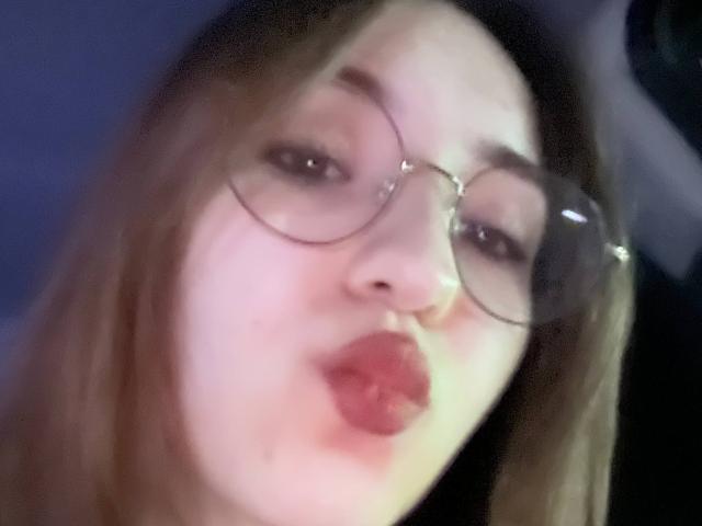 AletaBreslauer with pouty lips, wearing round glasses, has light skin and blonde hair, slightly blurry selfie showing her face and lips in a sensual, pouty expression.