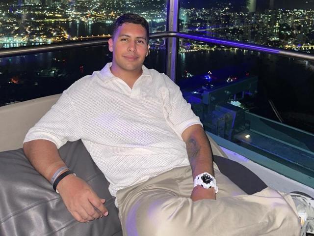 Sercho is a chubby dude with short brown hair, wearing a white striped polo and beige pants, sitting on a couch, looking at the camera with a slight smile.