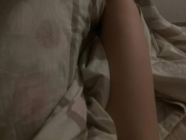 JuttaHillwig's leg is partially covered by a patterned bedsheet, showing a smooth, light brown thigh. The bedsheet has soft, muted colors and subtle, circular designs.