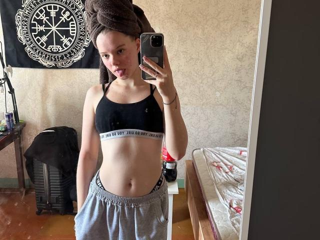 DominicaChambley with a towel on her head, black sports bra, and gray sweatpants, sticking out her tongue in a mirror selfie, showing her flat stomach and small tits.