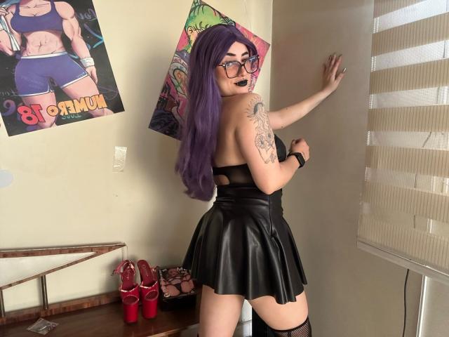 LilithDark69 with purple hair, glasses, black strapless leather dress, tattooed arm, black lipstick, looking back, standing by wall, red high heels on wooden table.