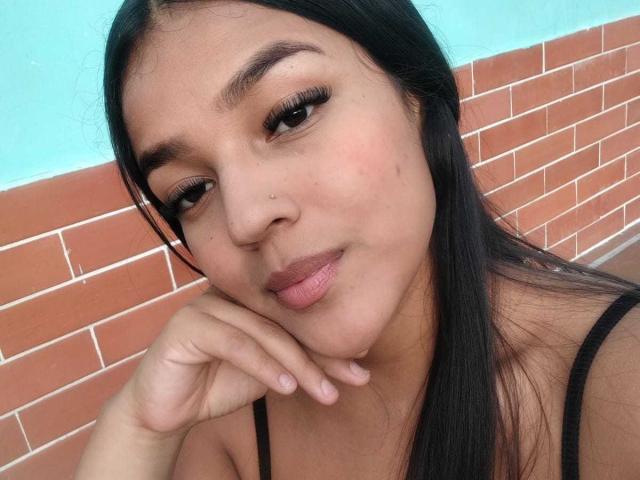 SheilaBrunette has long black hair, brown eyes, and a nose piercing. She's posing with her chin in her hand, showing off her pouty lips and cute ass.