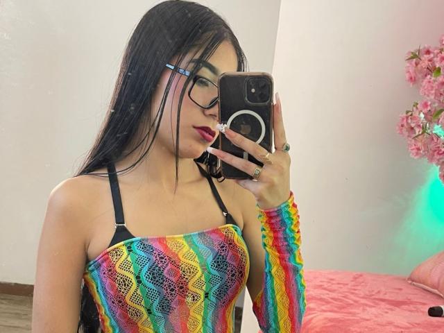 VioletaVelvet with long black hair, glasses, and rainbow crochet top, taking a mirror selfie with her phone, showing her tits in a strapless black bra.