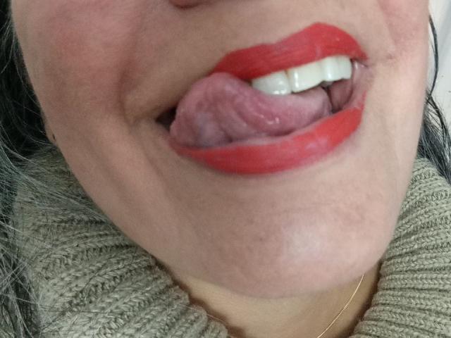 LailaCastillo's tongue is out, licking her upper teeth with bright red lipstick on her slightly parted lips, wearing a green textured scarf.