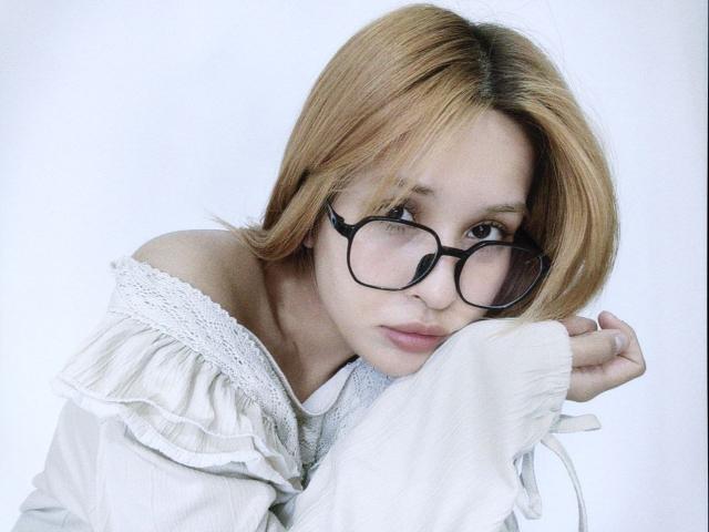 Chantell Houlihan, avec ses cheveux blonds, ses lunettes noires et son haut blanc à épaules dénudées, repose son menton sur sa main, l'air triste. Ses seins sont partiellement visibles sous la dentelle..