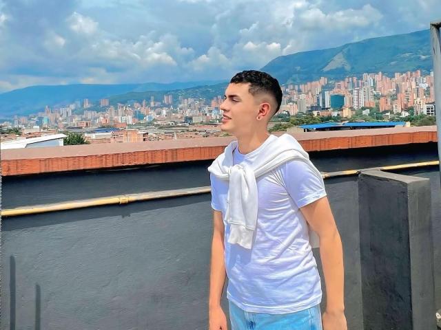 LordThoring with a white shirt, wet from sweat, has a white towel around his neck, standing on a rooftop, looking to the side, wearing blue jeans, short black hair.