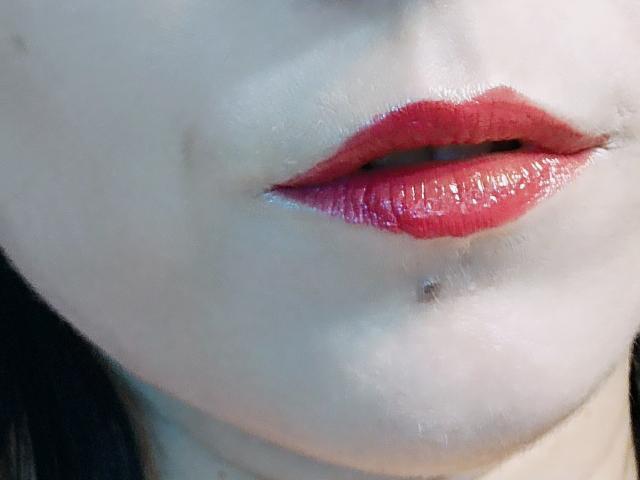 Os lábios vermelhos e brilhantes de OrianaLaFrancaise estão ligeiramente entreabertos, revelando um vislumbre de seus dentes. Ela tem uma pequena pinta abaixo do lábio inferior. Sua pele clara contrasta com o vermelho..