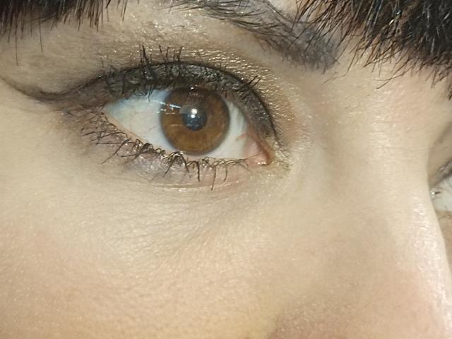OrianaLaFrancaise's brown eye with shiny gold eyeshadow, dark eyebrows, and slightly wet skin, showing a close-up of her right eye. Her eyelashes are long and curled.
