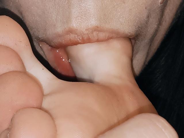 OrianaLaFrancaise's mouth is wrapped around her own toes, with her tongue touching the ball of her foot. Her lips are slightly parted, showing a wet, pink tongue.