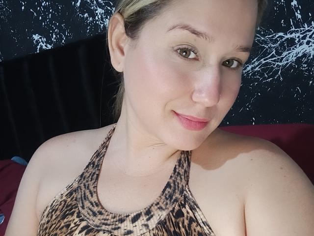AlexaHotSeins, con la pelle chiara, i capelli biondi e gli occhi marroni, indossa un top a halter con stampa leopardo, sorride dolcemente alla fotocamera, mostrando le spalle scoperte e un trucco leggero..