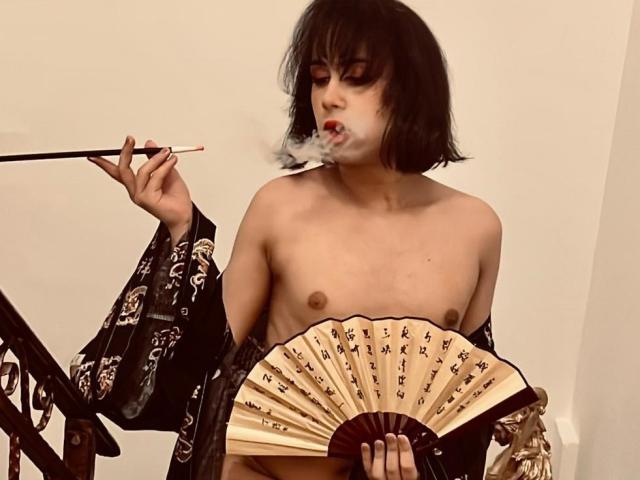 Topless FemCupid with short black hair, holding a fan and smoking a pipe, wearing a black kimono, exposing small tits and a flaccid tan line, standing on a staircase.