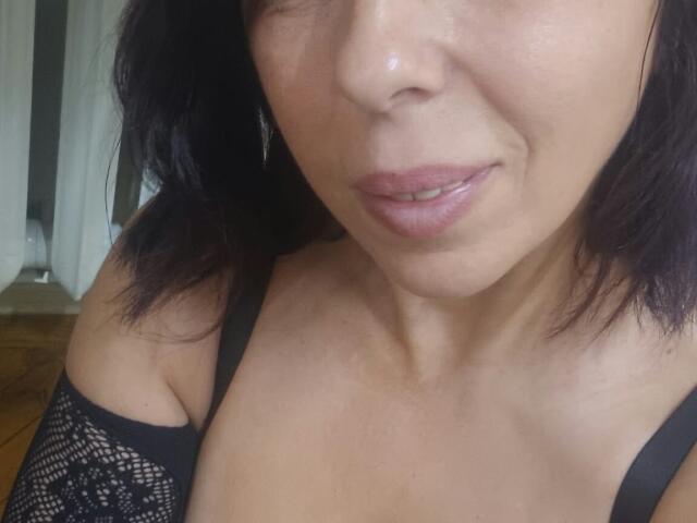 Il viso di LauraSin, con le labbra rosa leggermente dischiuse, i capelli scuri fino alle spalle e una maglia nera in pizzo con le spalle scoperte, che mette in mostra il suo seno piccolo e prosperoso. La sua pelle è di un color marrone chiaro..