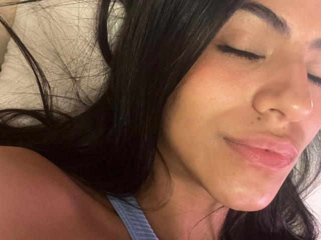 EvaGate's face, sleeping, with dark hair, closed eyes, pink lips, slight smile, nose piercing, and freckles, wearing a blue tank top, soft light, relaxed.