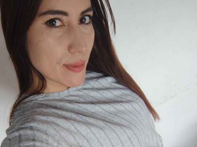 SofiaAnal with brown eyes, light skin, and straight brown hair, wearing a gray ribbed shirt, looking over her shoulder with a subtle smile. Her tits are small and unvisible.