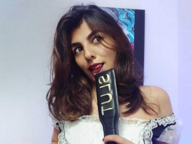 SoyVeronica with dark, wavy hair, holding a black award with "2017" in gold, wearing a white off-shoulder lace dress, tongue slightly out, looking playful.