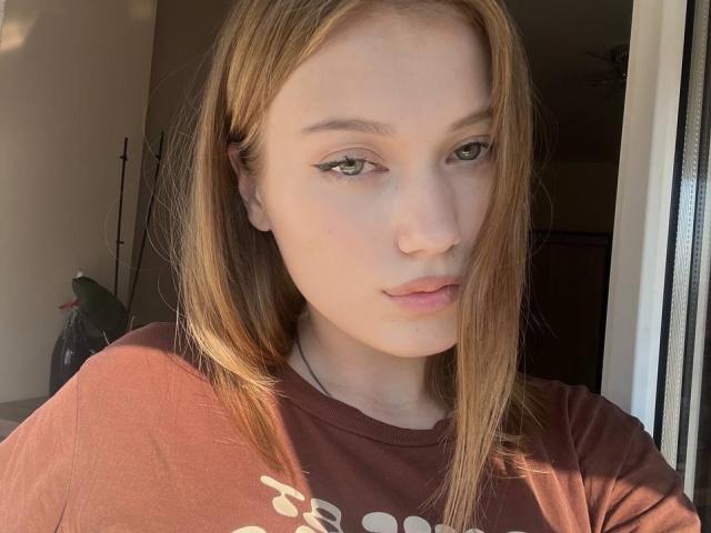 BobbyeWelson has pale skin, light brown straight hair, green eyes with winged eyeliner, and is wearing a brown shirt. She's looking to the side with a slight pout.