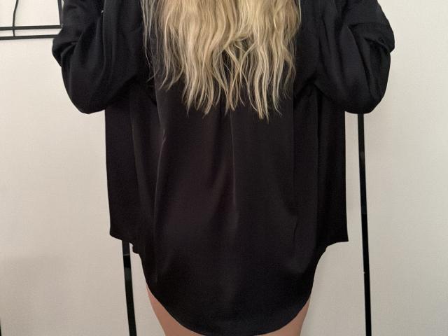 Das schwarze Seidenhemd von MysteryLaddy, langes, welliges blondes Haar, keine Hose, Hände erhoben, trägt schwarze Ärmel, weiches Licht, einfacher Hintergrund, Fokus auf den Oberkörper..