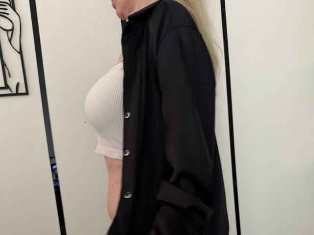MysteryLaddy's tits are visible in a white ribbed crop top under an open black shirt, showing a side profile with blonde hair and a slight belly.