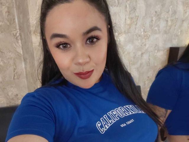 EveWillis has medium tits, brown eyes, and long black hair in a blue shirt, with red lipstick and a slight smile. She's looking at the camera.