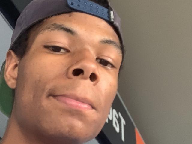 AndyCris has a medium brown skin tone, short dark hair, and a slight smile. He's wearing a backward blue baseball cap. His nose is large and his lips are pink.