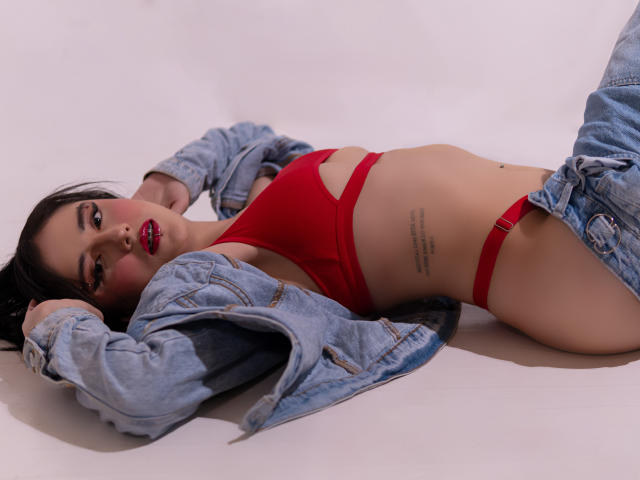 Valerie Banks sdraiata sulla schiena, indossa un top da bikini rosso e una giacca di jeans, mostrando un tatuaggio sul fianco, con i jeans abbassati, che rivelano il suo sedere scoperto..
