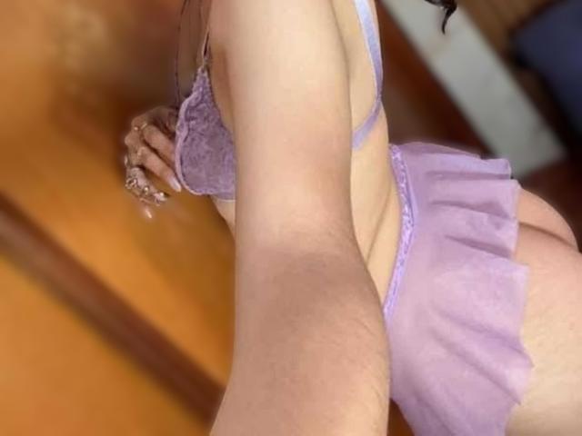 LunaValu in purple lace bra and sheer skirt, showing her ass and part of her tits, taking a selfie with her right hand. Her skin is light.