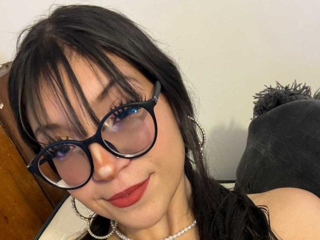LunaValu hat schwarzes Haar, blaue Augen, roten Lippenstift und trägt eine schwarze Brille mit großen Ohrringen. Sie lächelt leicht und hat ein kleines Nasenpiercing. Ihre Brüste sind nicht sichtbar..